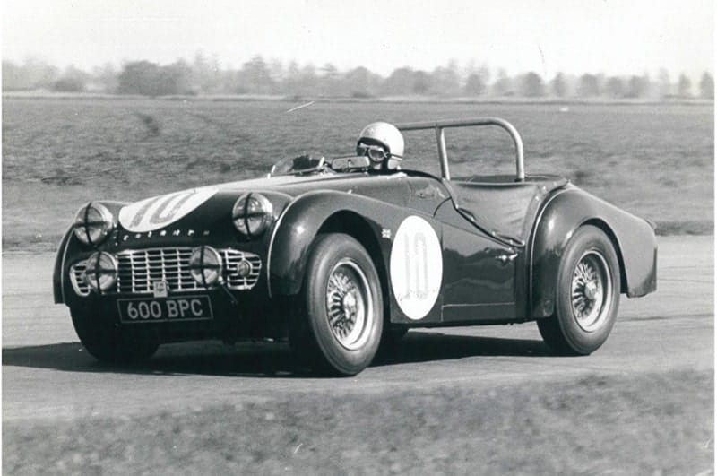 A vintage black and white photo of a classic sports car, possibly from the 1950s or 1960s, with the registration plate "600 bpc", racing on an expansive airfield.