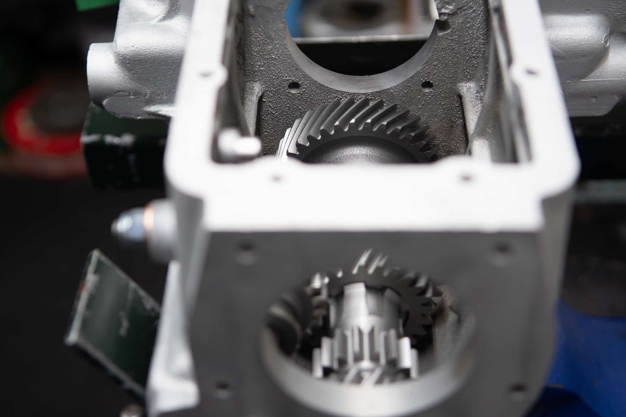 Close-up view of the internal gears of a mechanical device, possibly a gearbox or engine. The image focuses on the intricate metal gears and their alignment within a metallic housing. The gears exhibit fine engineering and detailed craftsmanship.